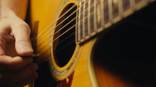 Young musician man sitting and playing acoustic guitar among music equipment in studio close-up. Guitarist plays melody